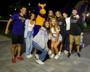 Students pose around someone dressed in an Ephelia the Cow costume during a night-time festival during First Days.